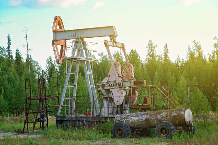 An abandoned oil or gas rocking machine against a blue sky, exhausted resource. Clogged field of gas and oil production.