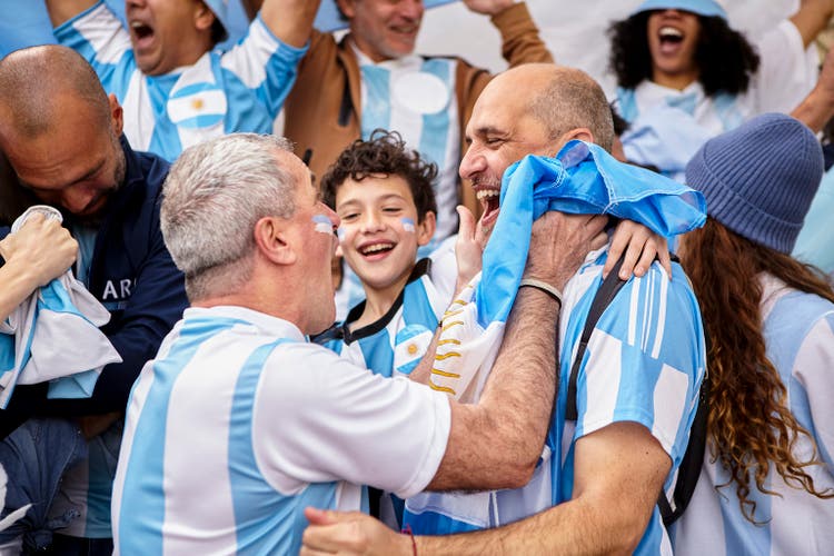 Argentinian football fan friends and little boy celebrating goal while standing in the crowd