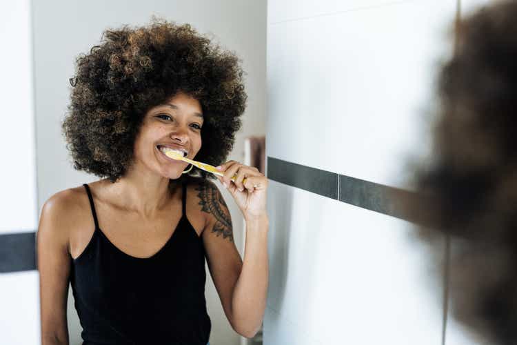 Многорасовая женщина чистит зубы в ванной комнате перед зеркалом