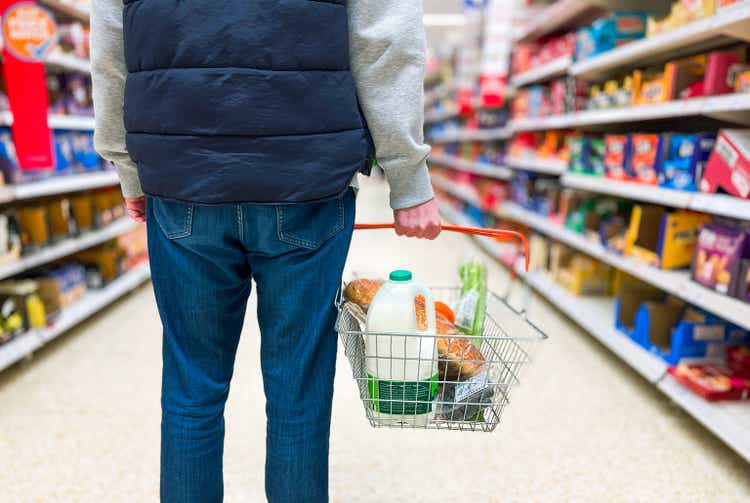 Man holding shopping basket with bread and milk groceries in supermarket