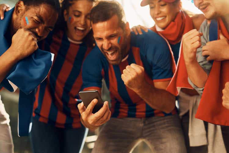 Excited soccer fans celebrating the winning goal of their favorite team while watching match on smart phone.