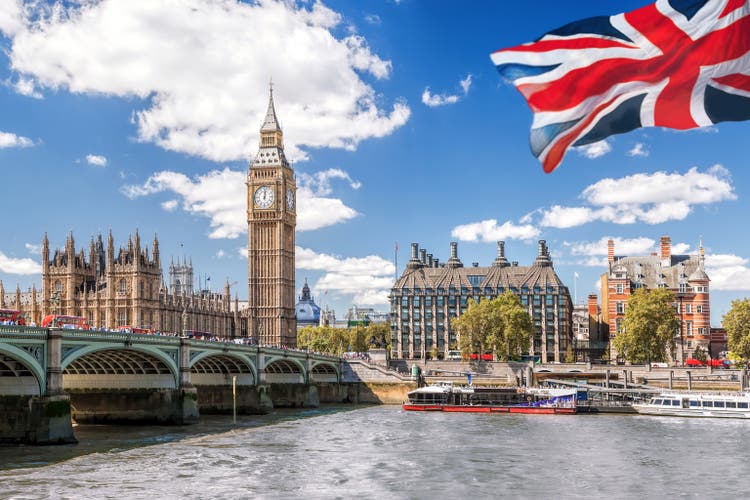 Big Ben with bridge over Thames and flag of England against blue sky in London, England, UK