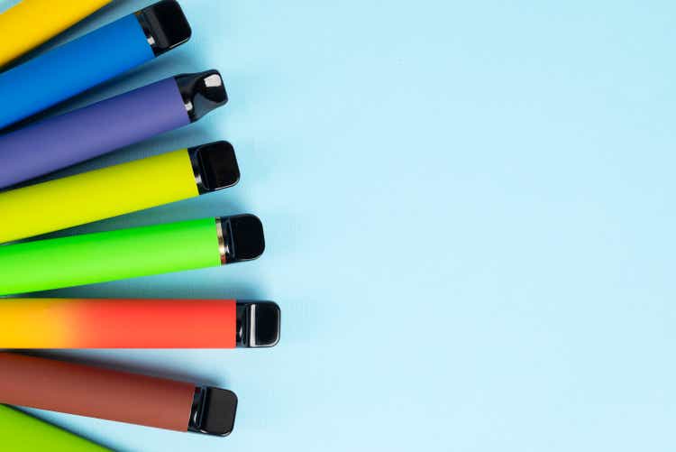 Layout of colorful disposable electronic cigarettes with shadow on blue background. Modern smoking, e-cigarette and nicotine concept.top view