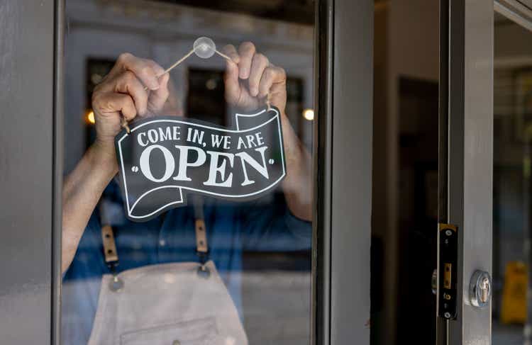 A business owner hangs an open sign on the restaurant door and closes it