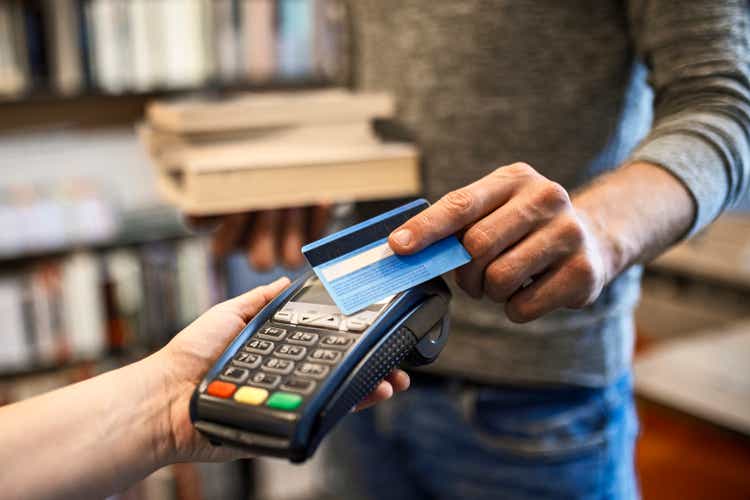 Unrecognizable person paying with a credit card for books at the modern bookstore
