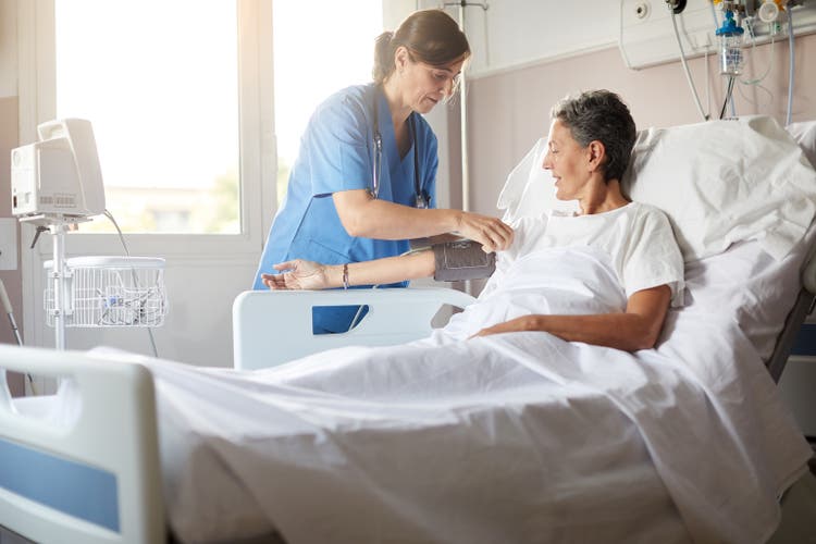 Female nurse adjusting the blood pressure monitor on female hospital patient