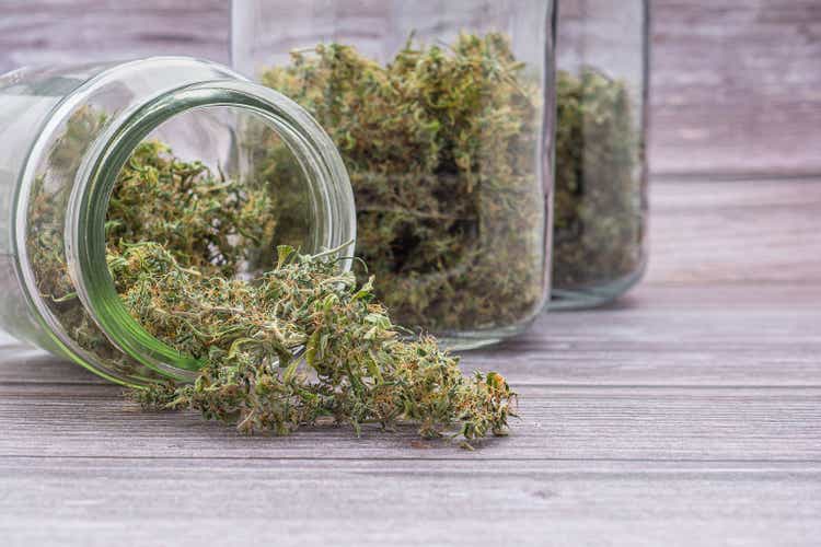 Cannabis buds pouring out of a container jar glass with two container jar glass background placed on wooden table
