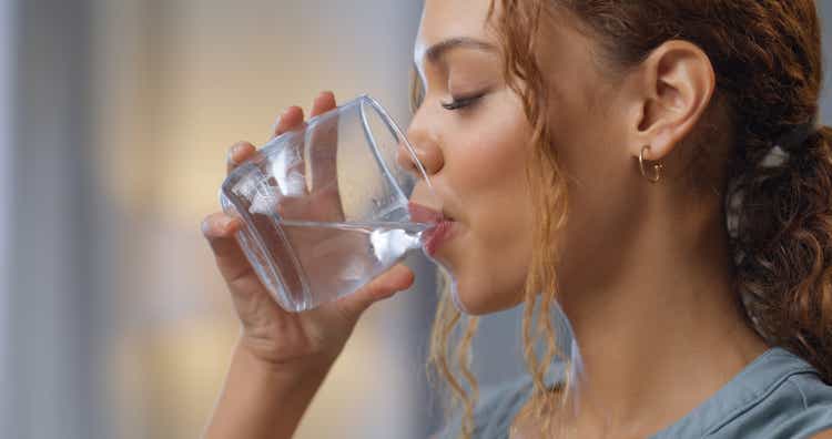 Gros plan d'une femme buvant un verre d'eau pour l'hydratation, la soif et la santé chez elle.  Fille heureuse avec un bien-être, un régime alimentaire et un mode de vie sain en profitant d'une boisson aqua fraîche tout en se relaxant à la maison.