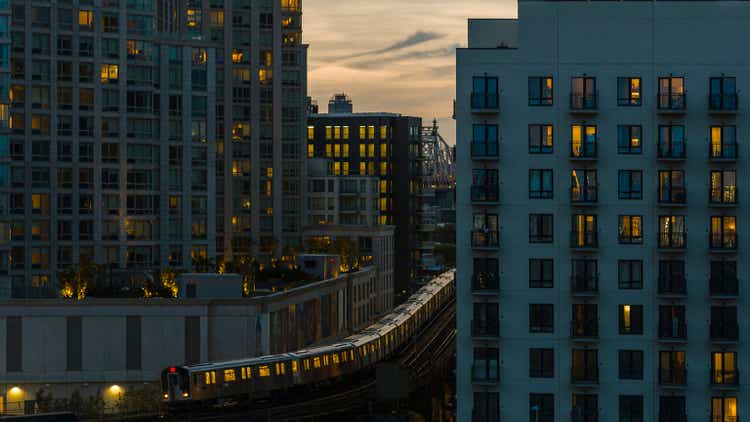 Train riding on the elevated subway line between buildings in Long Island City, Queens in the evening.