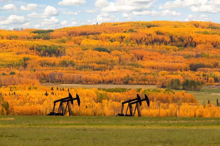 Pumpjacks in the agricultural field among beautiful fall scenery.
