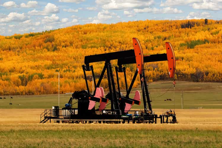 Pumpjacks in the agricultural field among beautiful fall scenery.
