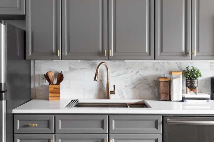 A grey kitchen with a gold faucet and marble subway tile.