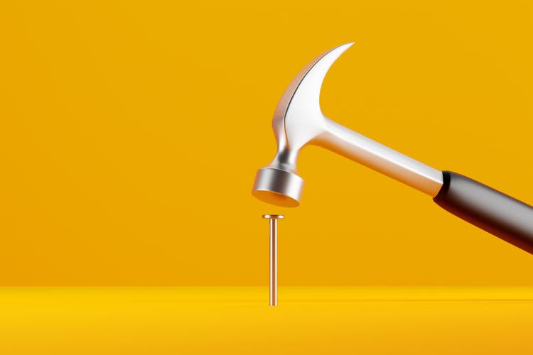 Claw hammer with black plastic handle hitting a nail on yellow background.