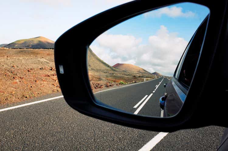 A road leading into the distance reflected in the rearview mirror in a volcanic landscape