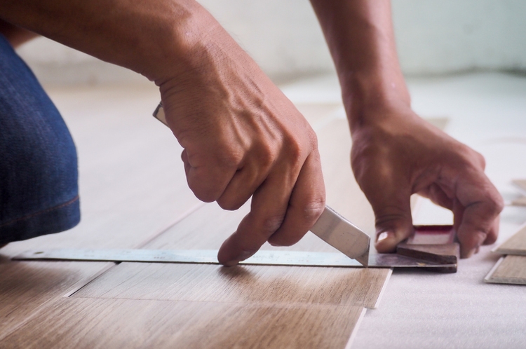 A technician is cutting luxury vinyl floor tiles with a cutter to lay the floor before placing it on the leveling foam.
