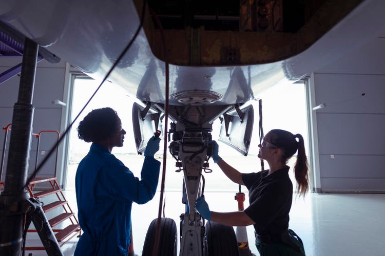 Female aircraft engineers inspecting landing gear on large jet