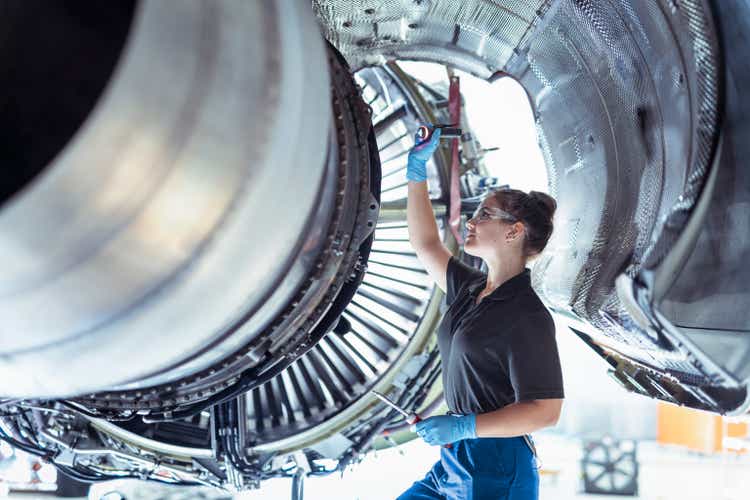 Female apprentice aircraft maintenance engineer work underneath jet engine