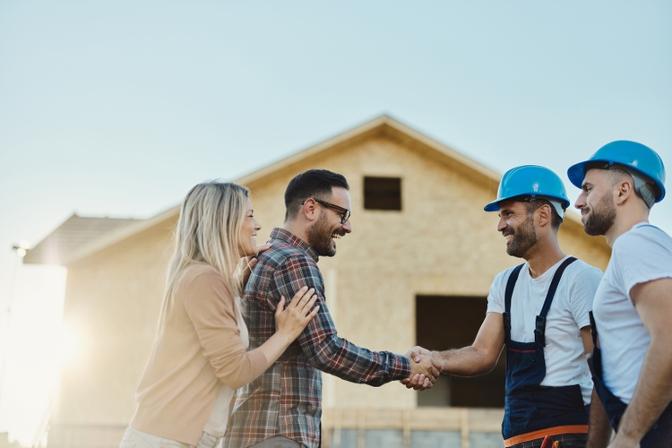 Happy couple greeting manual workers in front of renovating house.