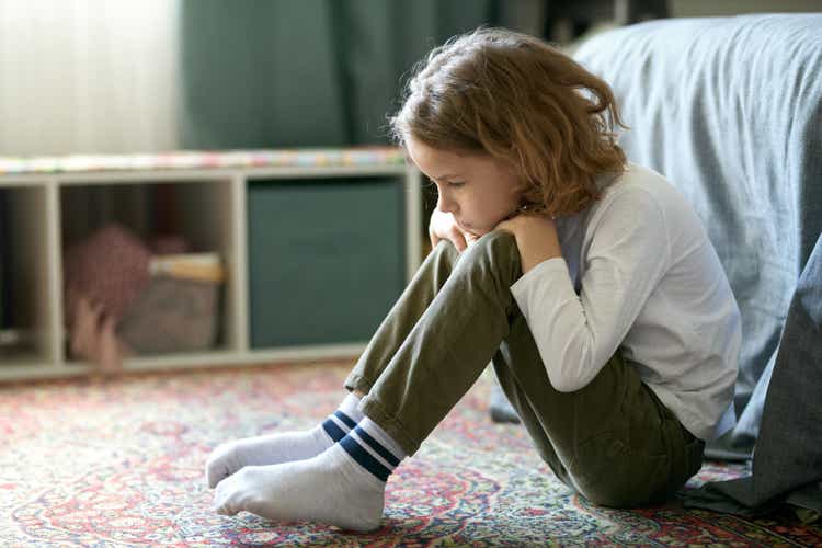 Kleiner Junge, der sich einsam fühlt, sitzt im Schlafzimmer