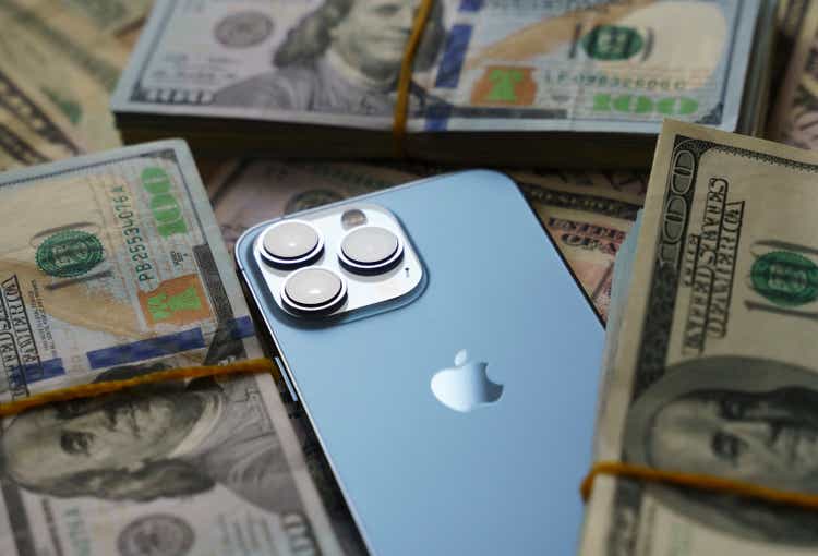 Apple iPhone 13 Pro smartphone with camera lenses stands over US Dollar banknotes