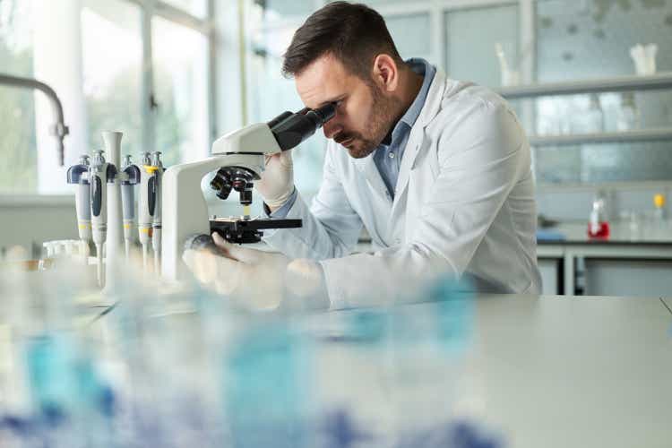 Young male chemist examining medical sample through a microscope in laboratory.