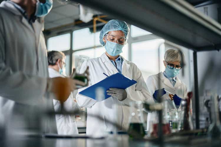 Black scientist taking notes while working with her colleagues in laboratory.