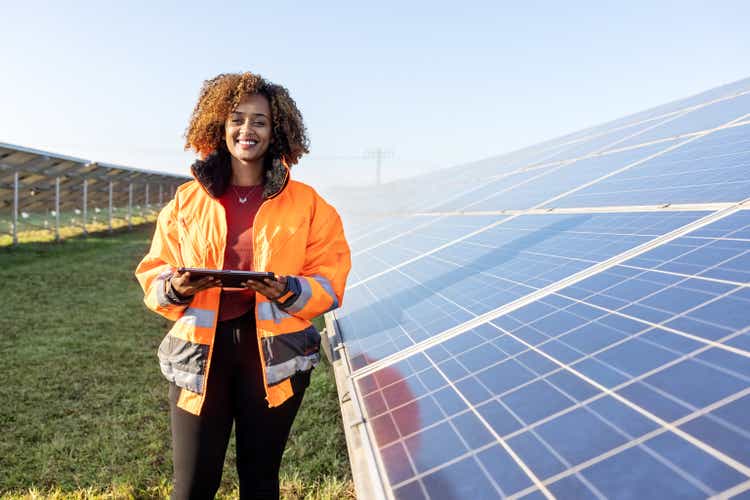 Technician holding a digital tablet standing by solar grid at solar farm