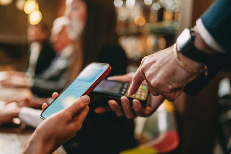 Close up shop of the hand of a woman paying with her smart phone at the restaurant