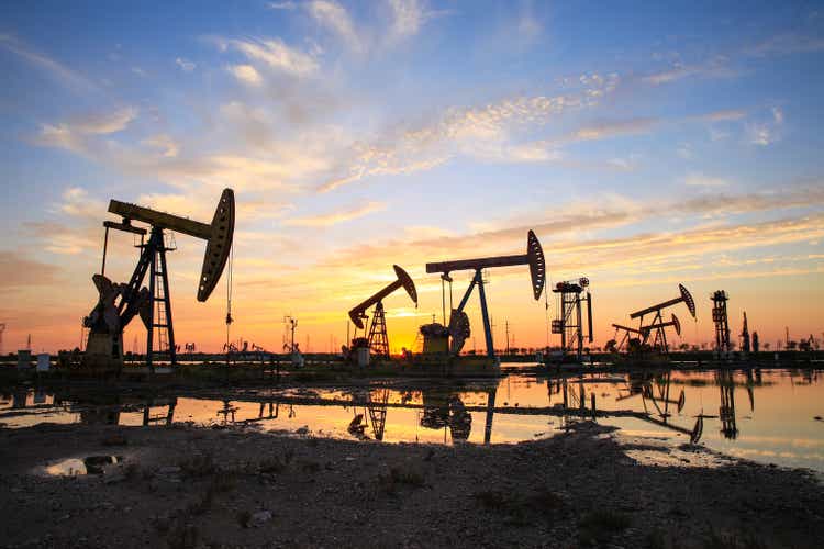 Oil field site, in the evening, the oil pump is running, the oil pump and the beautiful sunset are reflected in the water