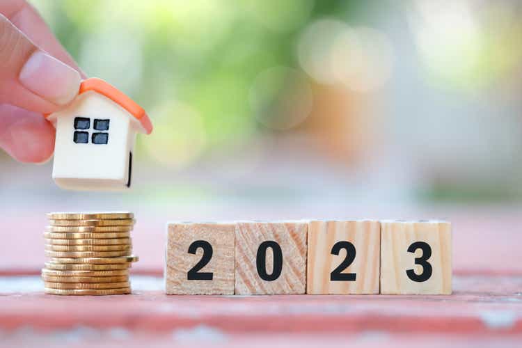 2023 Happy New Year. Business and saving money for buy property, Financial growth, loan, mortgage, sale price and home tax. Hand holding house model on coins stack and wooden blocks number 2023.