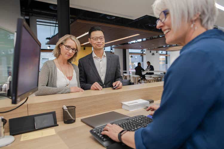 Bank teller at computer helping couple at bank branch counter