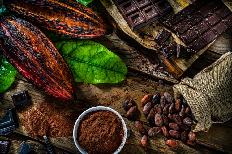Dark chocolate bars, cocoa pods and cocoa powder on rustic wooden table.