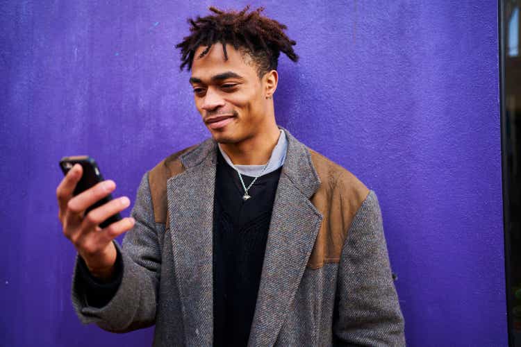 Fashionable man looking at his phone shot against a purple wall in the city