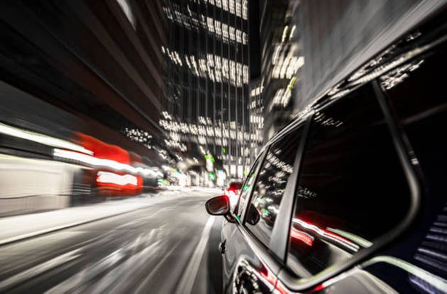 Shiny black electric car drives through the nightly big city of San Francisco.