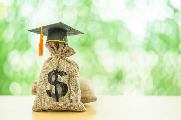 Education or student loan, financial aid and scholarship concept : Mortarboard or graduation cap on top of a US dollar cash bag. Depicting financial assistance for a student"s tuition and other costs.