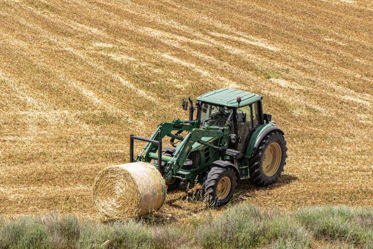 High angle shot of John Deere tractor lifting a hay bale in an open field in Italy