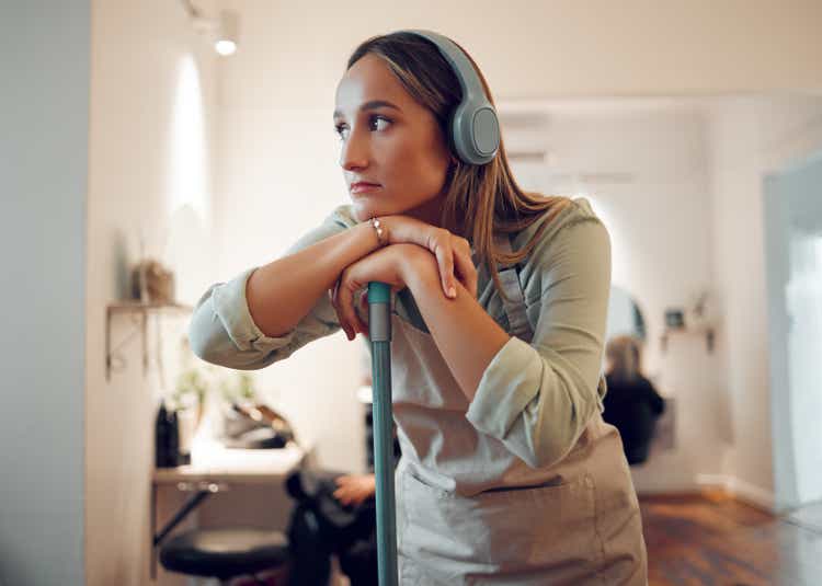 Woman, cleaning and tired with music in headphones while cleaning room in home. Cleaner, thinking and contemplating while listening to radio, podcast or streaming with rest, exhausted and burnout