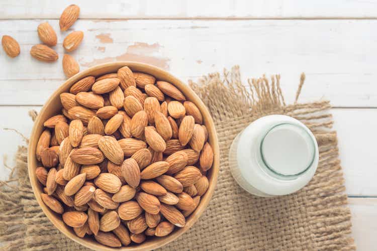 Almond milk in the glass with almond in the wooden bowl on the wooden table.