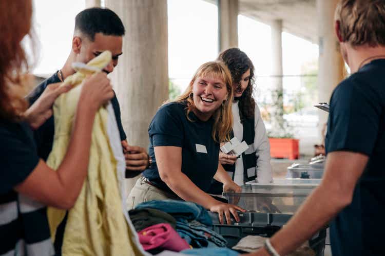 Happy female volunteer looking at colleague while sorting clothes at community service center