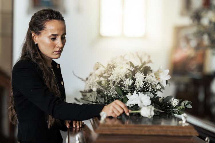 Funeral, sad and woman with flower on coffin after loss of a loved one, family or friend. Grief, death and young female putting a rose on casket in church with sadness, depression and mourning