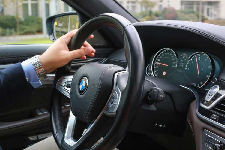 Man is driving car in city. BMW 7 Series central console panel, car steering wheel close-up.