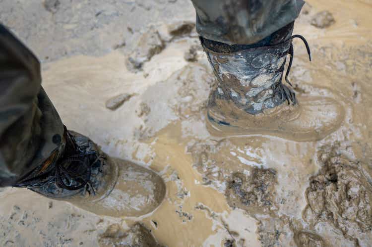 Close-up for a man"s legs in military camouflage with a trekking wellington shoes dirty in mud