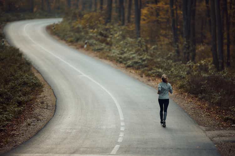 Rear view of a female athlete jogging on the road in nature.