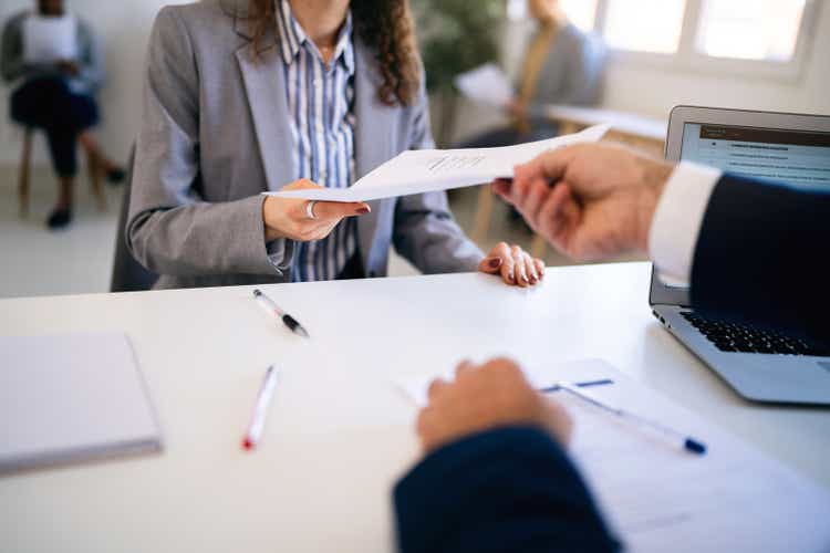Female candidate, handing to a recruiter her resume during job interview