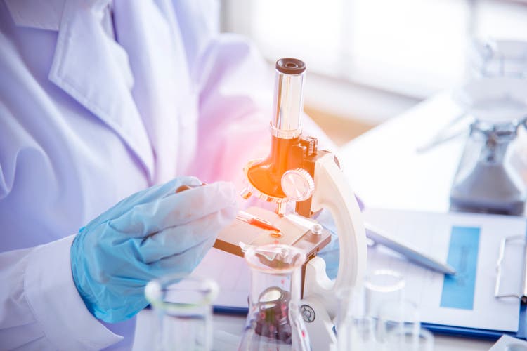 Woman scientist hand write note information in medical lab look at science microscope medical test, research biology chemistry. Asian Females technician laboratory analyzing blood test pharmaceutical