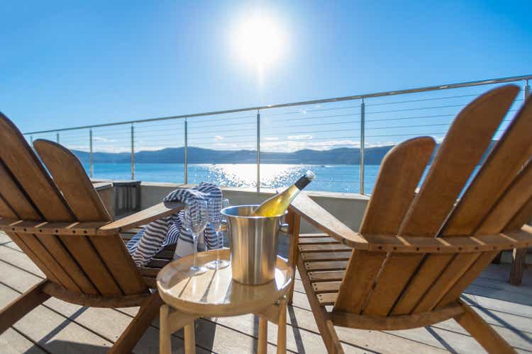 Two deck chairs on a waterfront balcony. There is an ice bucket with wine and glasses