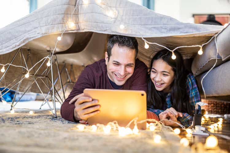 Father and daughter watching a movie on digital tablet in homemade fort