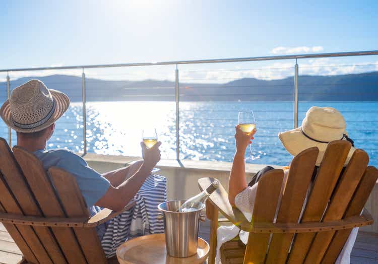 Couple relaxing and drinking wine on deck chairs in an over water bungalow.