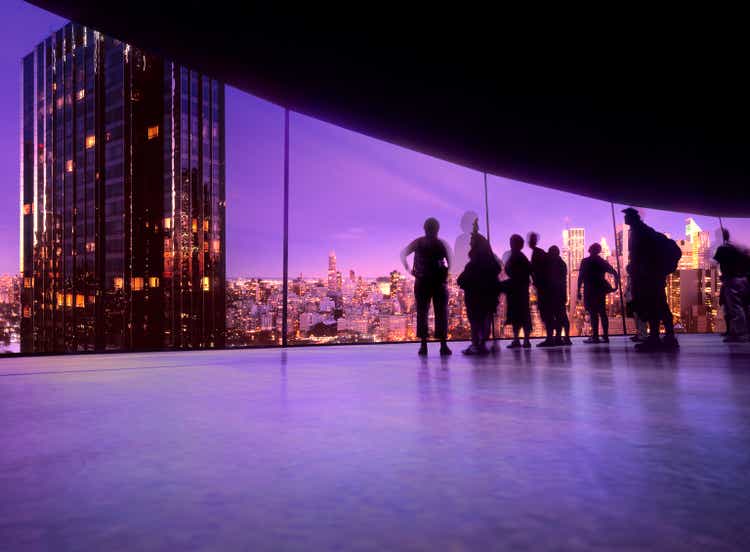 People watching the New York skyline reflected on a large curved screen