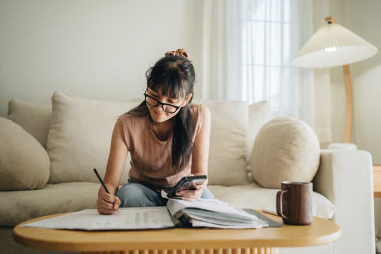 Asian woman planning budget and using calculator on smartphone.